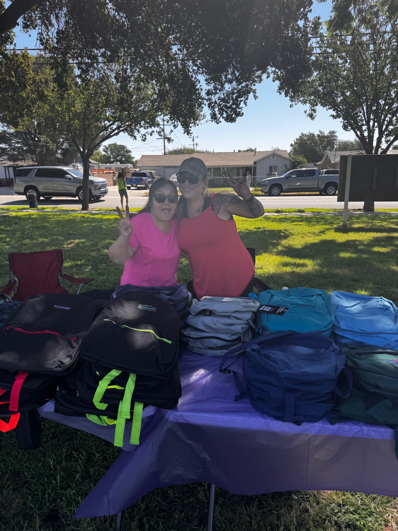 Volunteers smiling behind a table of backpacks at a community giveaway